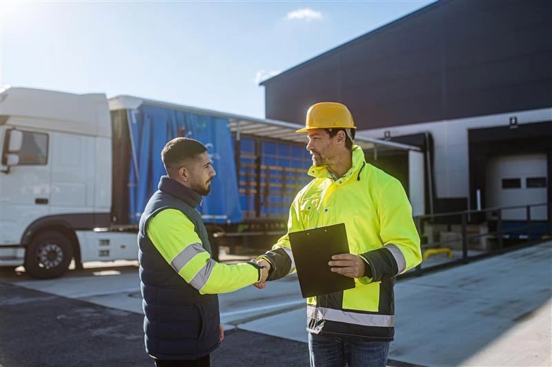 Two workers in flourescent yellow jackets shaking hands.