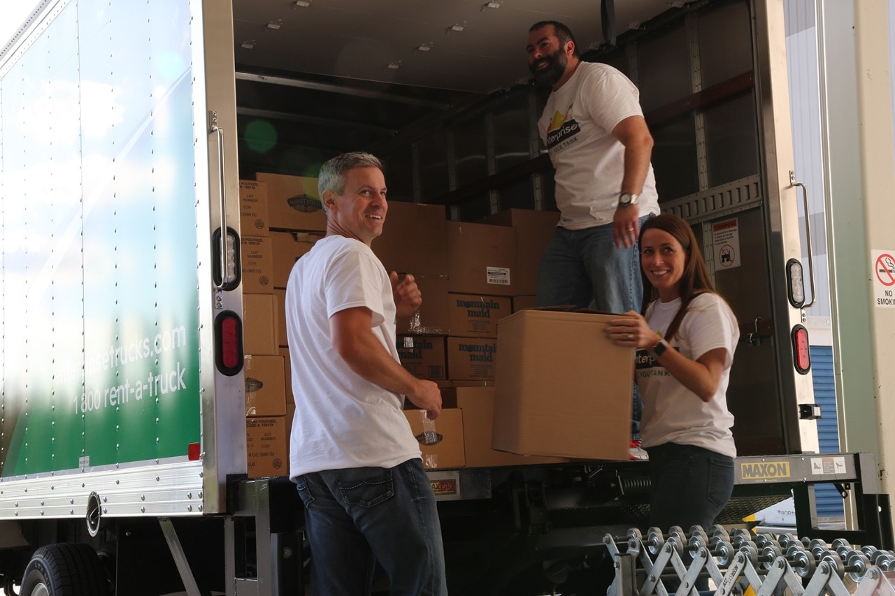 3 people unloading a box truck full of boxes.