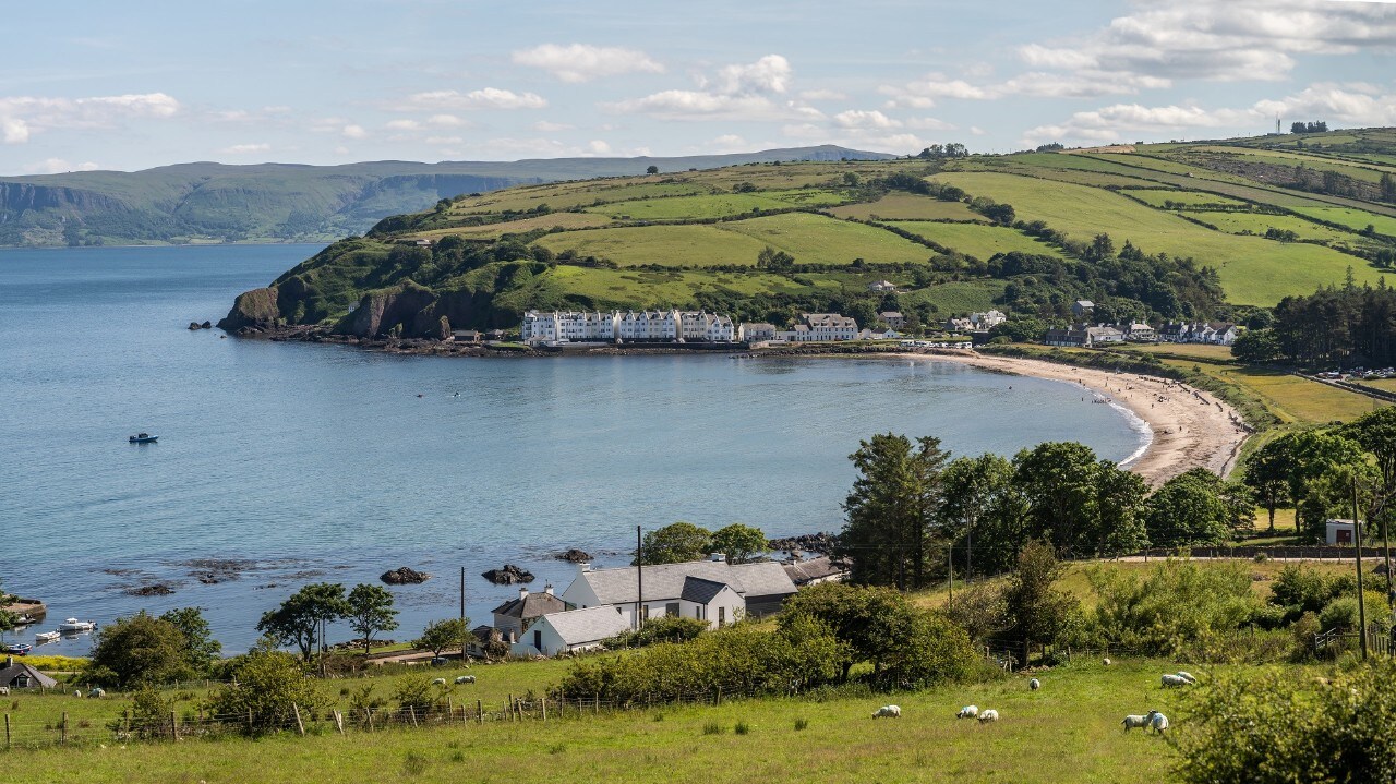 The bay at Cushendun, County Antrim, Northern Ireland on a warm sunny day with beach in view and distant houses abd hills. The area is on the causeway coast and is a popular tourist attraction