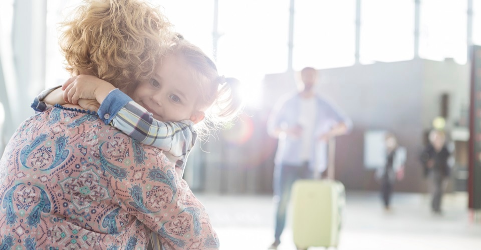 Mother and daughter hugging at the airport with father in background