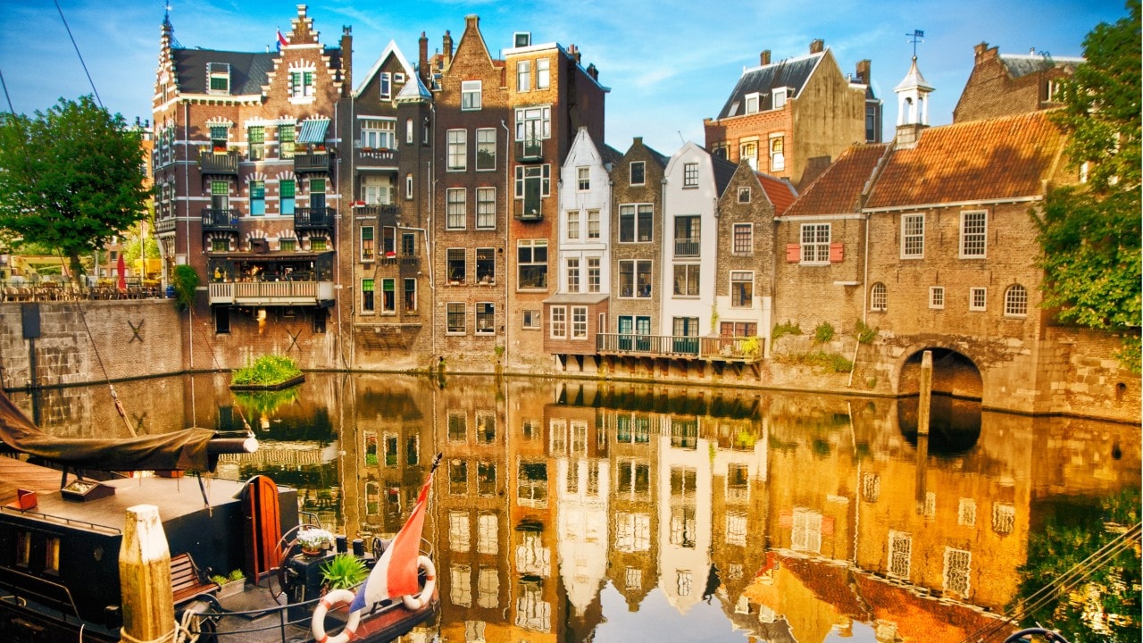 Historic cityscape along a channel in Delfshaven, a district of Rotterdam, the Netherlands. Visible are typical dutch architecture, historic sailing boats, restaurants, colorful reflection in the river, blue and dramatic cloudscape and beautiful sunset atmosphere.