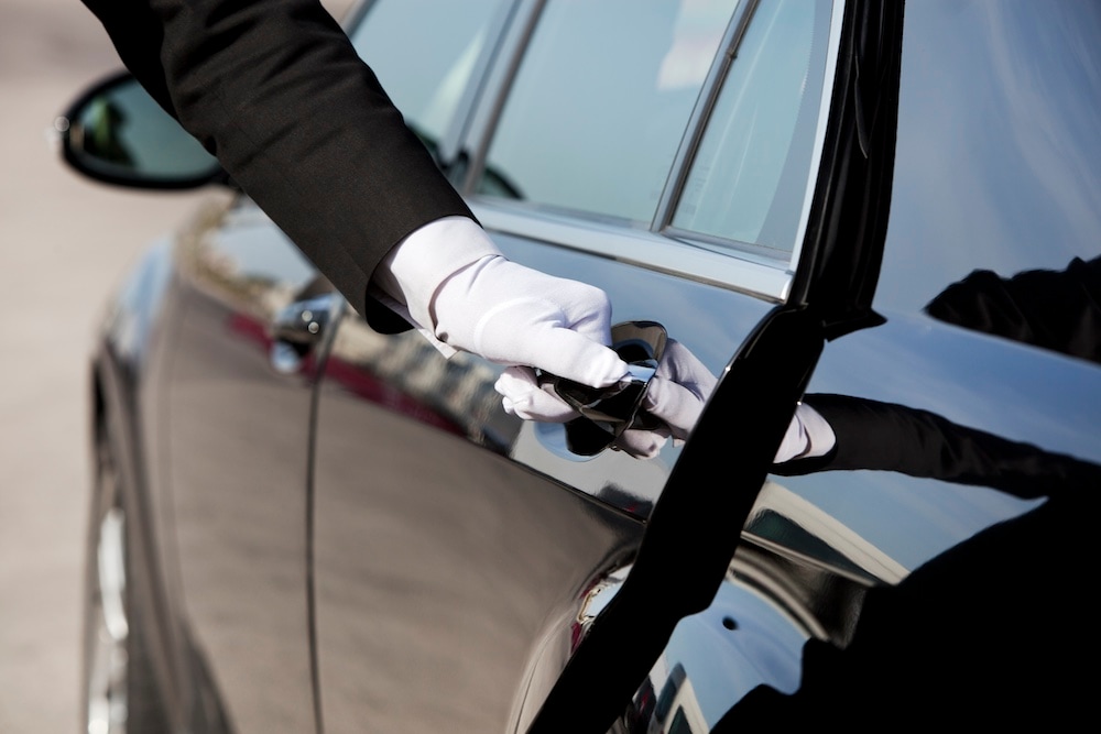 The white gloved hand of a uniformed chauffeur / doorman opening / closing a luxury car door.