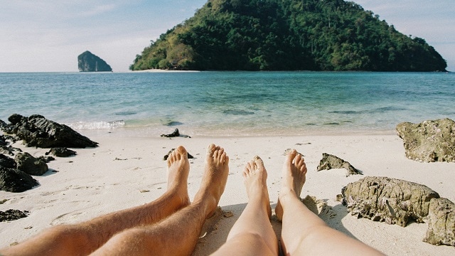 Couple's barefoot resting on the beach in Thailand. The view on another island Ko Kai, Chicken island in the distance. The beach is sandy with rocks scattered nearby. Thale Waek, Krabi, Thailand.
